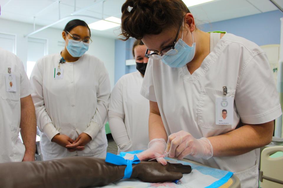 Katie Behrendt, a  nursing student at Glen Oaks Community College, surrounded by her classmates, practices inserting an IV.