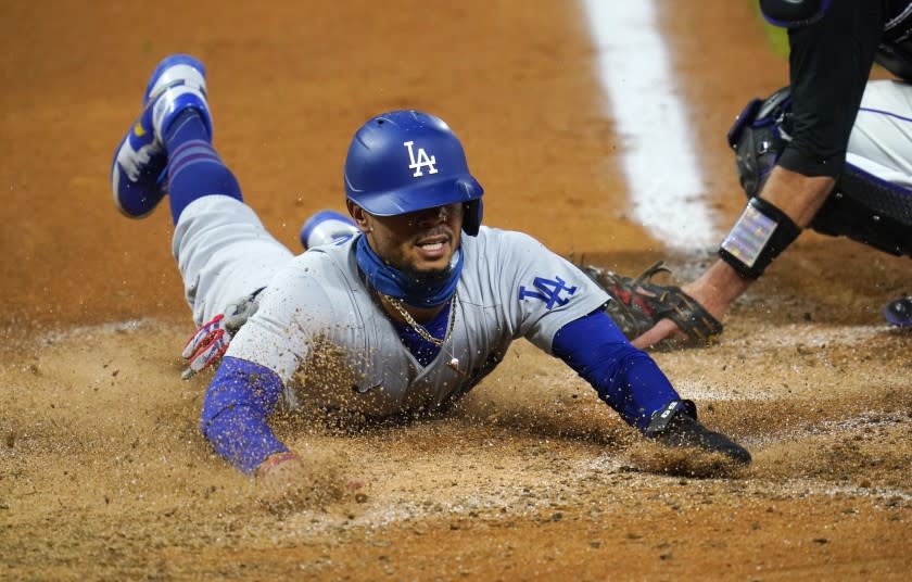 Los Angeles Dodgers' Mookie Betts scores after a pickoff throw to hold Betts at second base went awry from Colorado Rockies relief pitcher Mychal Givens during the seventh inning of a baseball game Saturday, Sept. 19, 2020, in Denver. Colorado Rockies catcher Drew Butera is at right. (AP Photo/David Zalubowski)