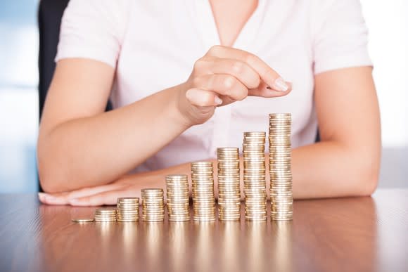 Woman stacking gold coins into rising piles on a table.