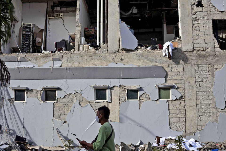 A man walks past a building damaged in Friday's earthquake in Mamuju, West Sulawesi, Indonesia, Monday, Jan. 18, 2021. Aid was reaching the thousands of people left homeless and struggling after an earthquake that killed a number of people in the province where rescuers intensified their work Monday to find those buried in the rubble. (AP Photo/Yusuf Wahil)