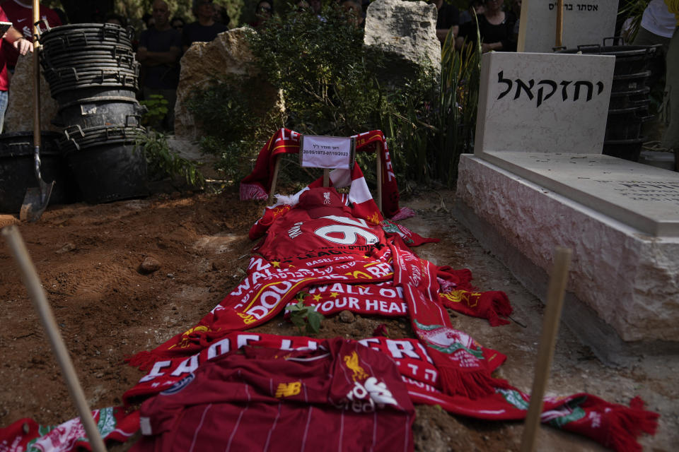 Mourners lay Liverpool FC shirts and scarfs on the grave of their friend and team fan Roee Munder, during his funeral in Kibbutz Metzer, Israel, Sunday, Oct. 22, 2023. Munder was killed by Hamas militants at his house in Kibbutz Nir Oz near the border with the Gaza Strip. On Oct. 7, more than 1,400 people were killed and more than 200 captured in an unprecedented, multi-front attack on Israel by the militant group that rules Gaza. (AP Photo/Ohad Zwigenberg)