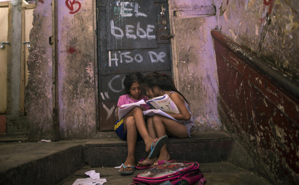 In this April 5, 2020 photo, Grace Lopez and Iunzu Asca do their homework sitting on a stoop inside the deteriorating building where they live, nicknamed “Luriganchito” after the country’s most populous prison, in Lima, Peru. The building is a relic from the area's historic era. But inside its now-cracked walls is a warren of narrow, dark passageways that smell of damp clothing and marijuana. (AP Photo/Rodrigo Abd)