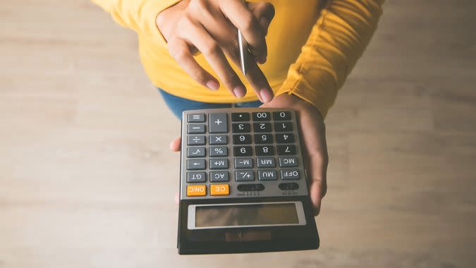 Woman entrepreneur using a calculator with a pen in her hand, calculating financial expense at home office.