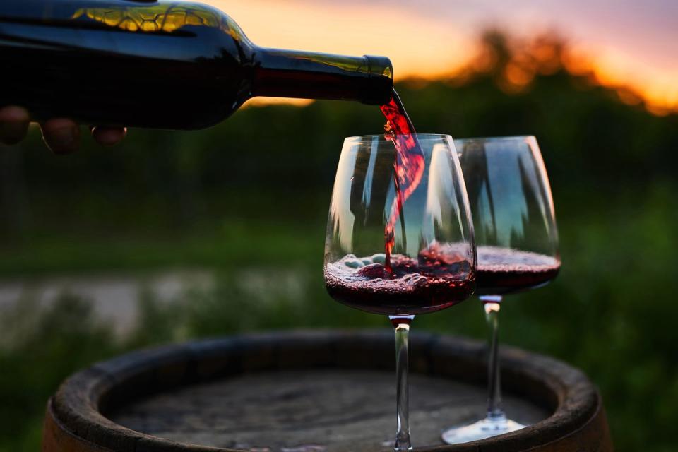 pouring red wine into glasses on the barrel
