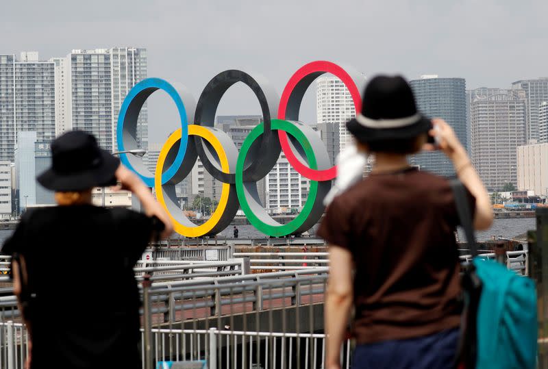 FILE PHOTO: Women look at the giant Olympic rings, which are being temporarily removed for maintenance, at the waterfront area at Odaiba Marine Park in Tokyo