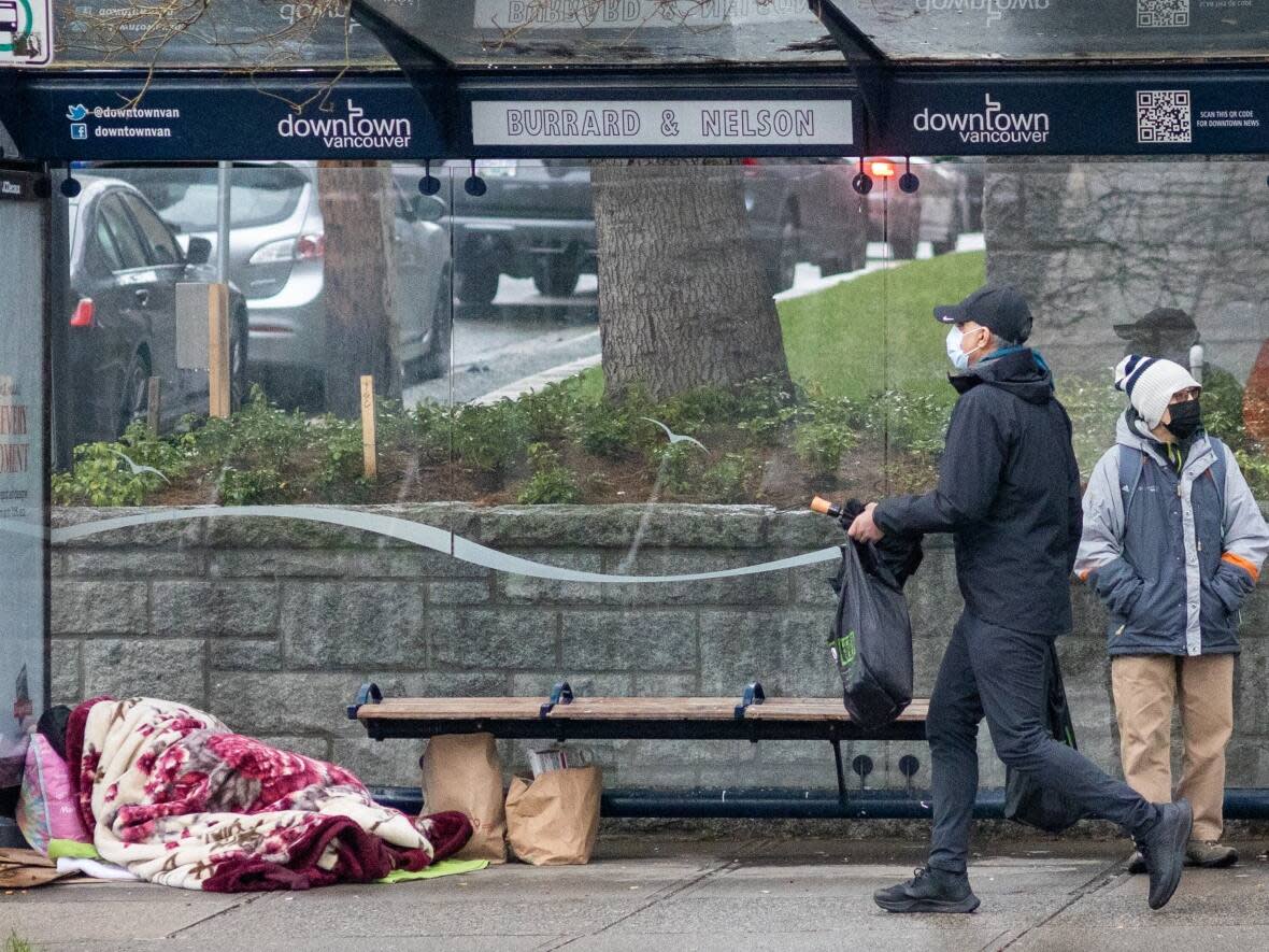 A person finds shelter for the evening in a bus stop on Burrard Street in downtown Vancouver.  An extended cold snap has settled over the province and there are concerns for the homeless population.  (Andrew Lee/CBC - image credit)