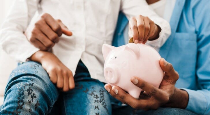 Image shows a parent and child sitting together and putting money into a piggy bank.