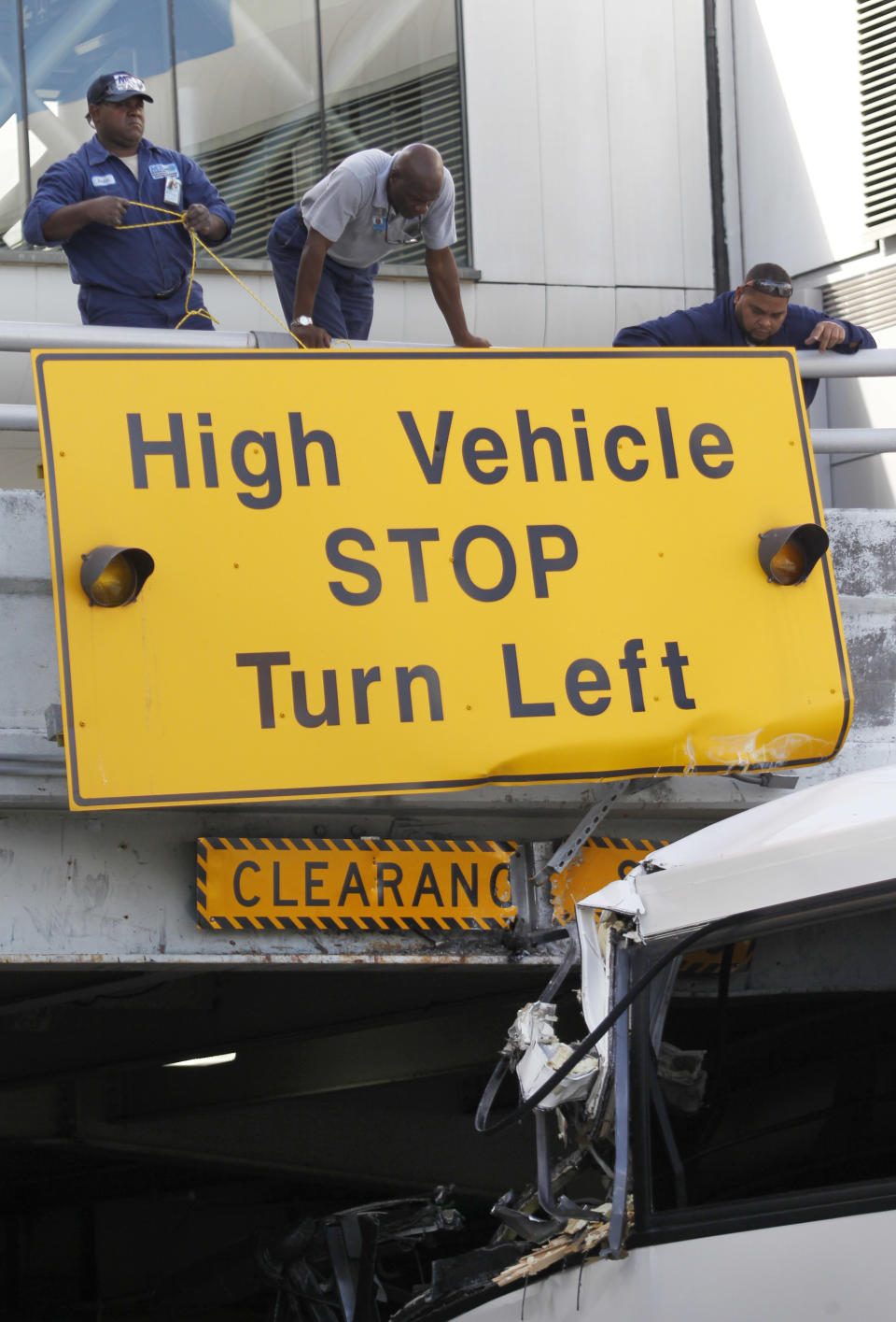 Airport workers secure a sign after a bus hit a concrete overpass at Miami International Airport in Miami on Saturday, Dec. 1, 2012. The vehicle was too tall for the 8-foot-6-inch entrance to the arrivals area, and buses are supposed to go through the departures area which has a higher ceiling, according to an airport spokesperson. (AP Photo/Wilfredo Lee)