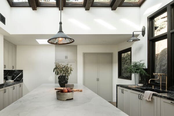 In the kitchen, a central island of White Macaubas Quartzite sits below vaulted skylights. "Marble counters and ledges create a sophisticated atmosphere, complemented by custom oak cabinetry and sourced brass fixtures, and an Ilve stove,
