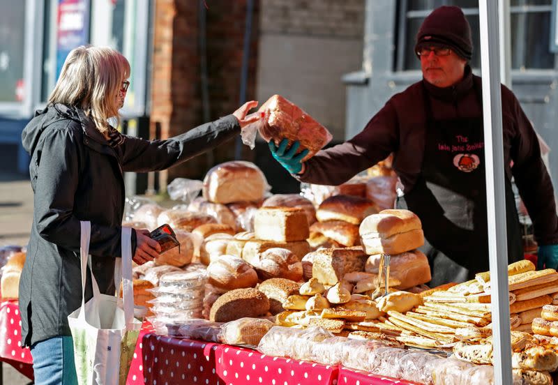 A lady buys bread from a market stall in Buckingham, Britain