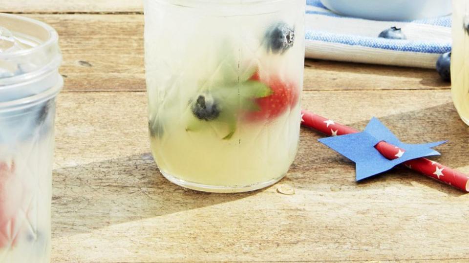 old fashioned lemonade in mason jars with fresh berries and paper straws on a wooden table outside
