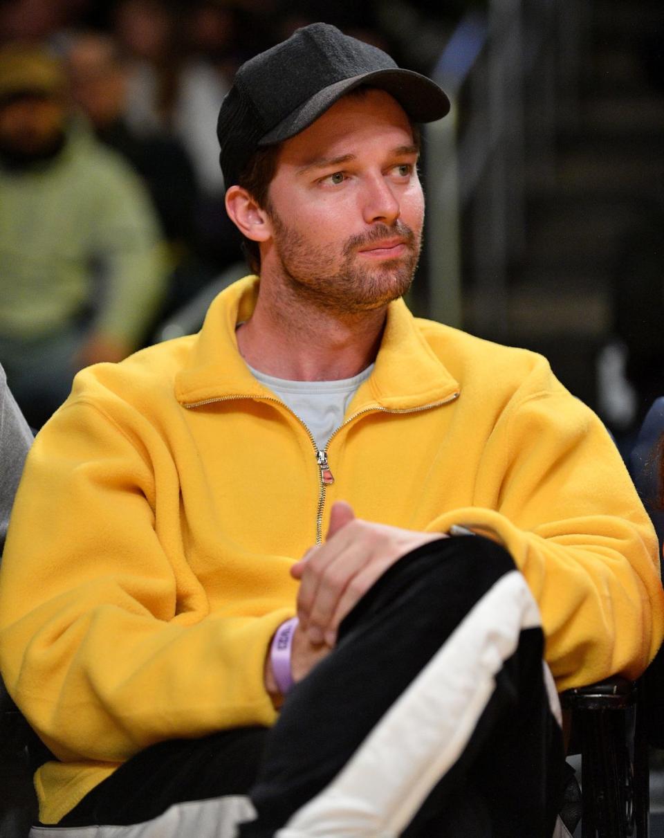 patrick schwarzenegger looking off camera as he sits with his legs folded