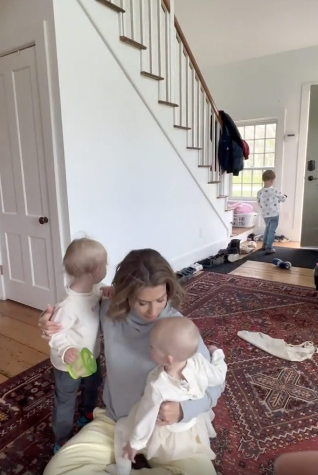 Hilaria holding two babies and a small child standing by the door in a house