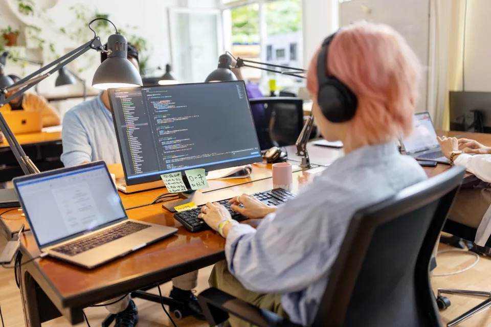A software engineer wearing headphones while sitting at a desk and coding on a computer.