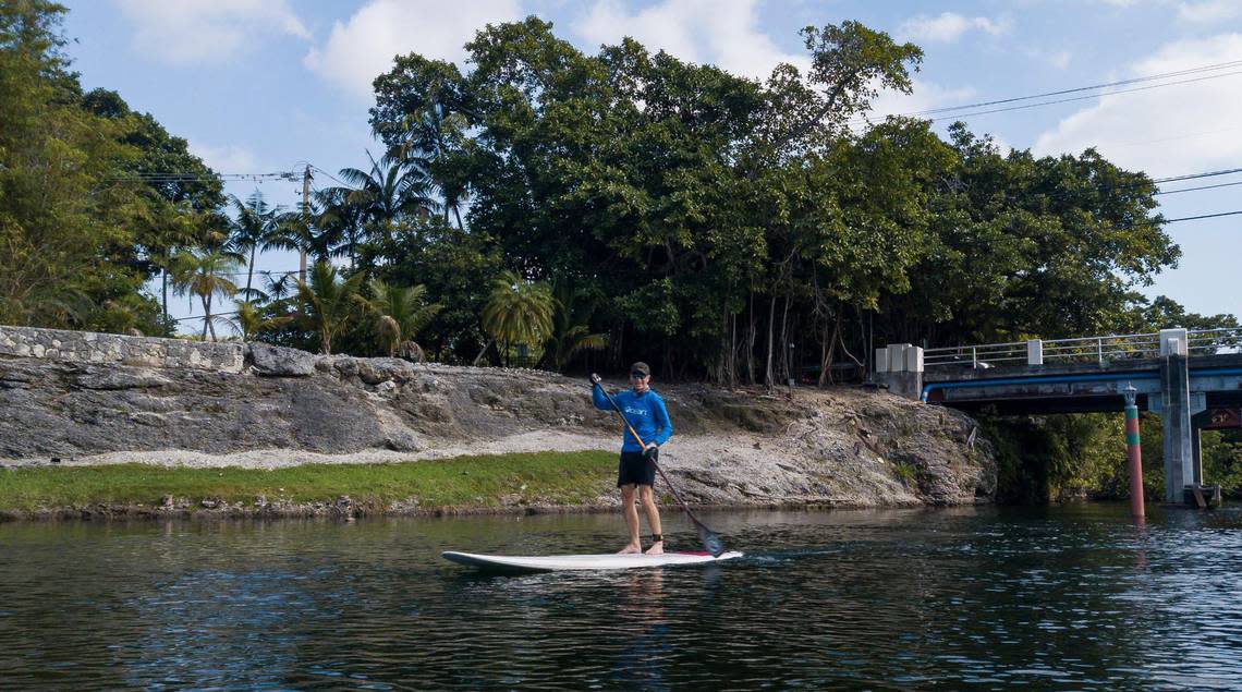 A man rides a paddle board down a canal near Cocoplum Plaza Circle on Dec. 12, 2022, in Miami. The canal is located near one of Miami-Dade County’s highest points of elevation.