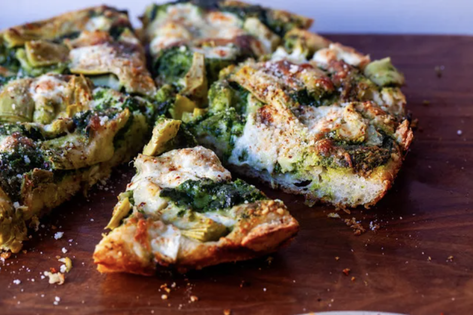 Sliced pesto pizza with toppings on a wooden surface