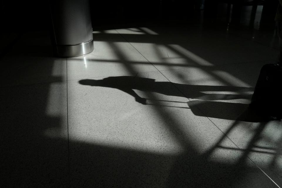 The shadow of a traveler pushing a suitcase is cast on the floor inside Miami International Airport, Monday, Dec. 27, 2021, in Miami. Thousands of flights worldwide were canceled or delayed on Monday, as airline staffing shortages due to the rapid spread of the omicron variant of COVID-19 continued to disrupt the busy holiday travel season.