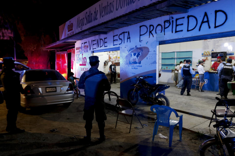 Police inspect a bar with the Spanish message "This property is for sale" is spray painted across it, where men play pool in San Pedro Sula, Honduras, Wednesday, May 1, 2019. Honduras' second city is where caravan after caravan of migrants have formed in recent months to head north toward Mexico and the United States, fleeing violence, poverty, corruption and chaos. (AP Photo/Delmer Martinez)