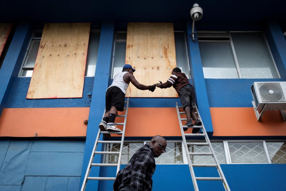 Two people board up the windows of an office building in Kingston, Jamaica on Wednesday as Hurricane Beryl approaches (REUTERS)