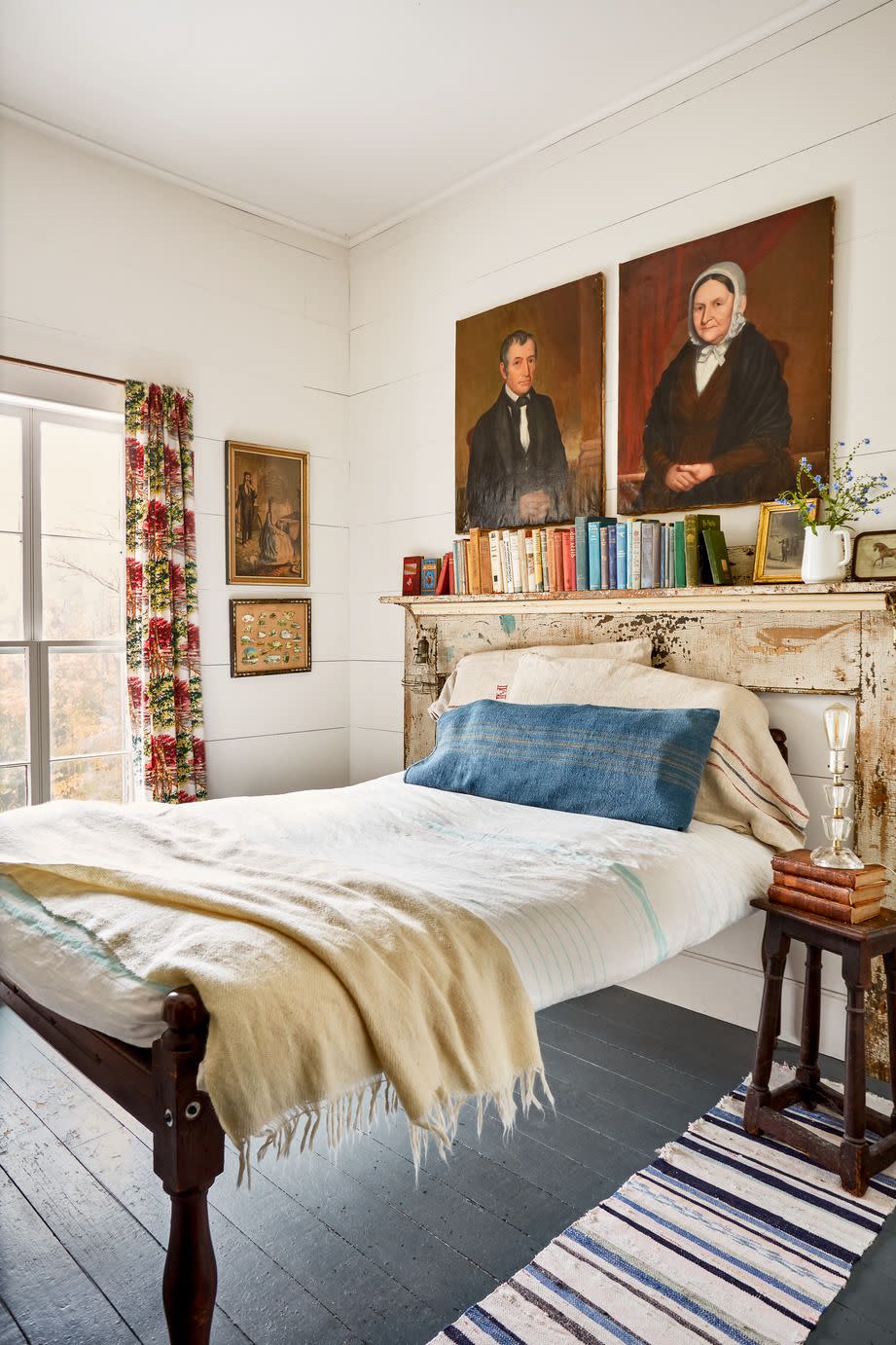 a small bedroom is packed with soulful touches like floral barkcloth curtains and a pair of antique portraits over the ned and a chippy mantel that acts as a second headboard