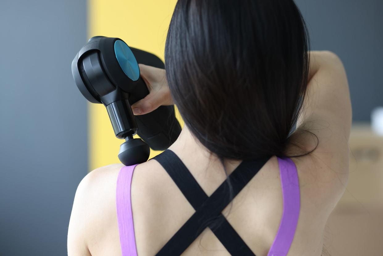 Woman doing massage of muscles of neck and back with percussion massager closeup. Recovery after sports training concept