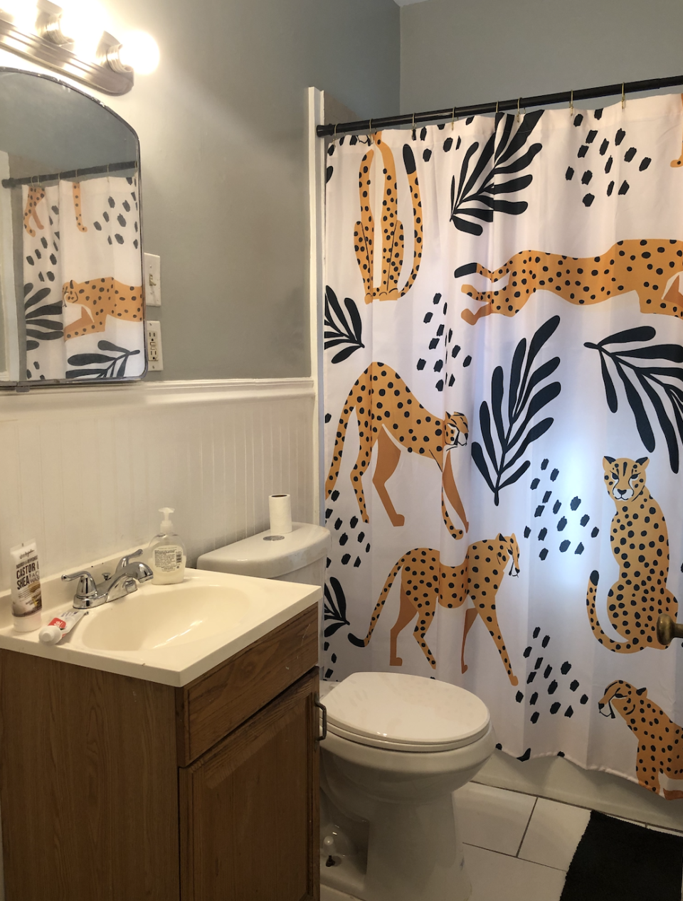 A bathroom with a wooden vanity, sink, toilet, and a shower curtain featuring various cheetah illustrations