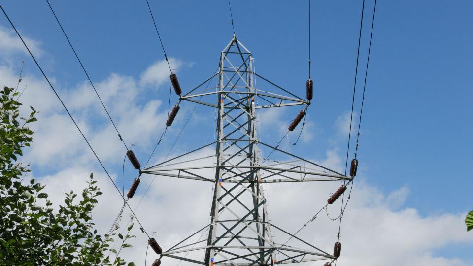 Pylon and powerlines against blue sky.. UK.  2023