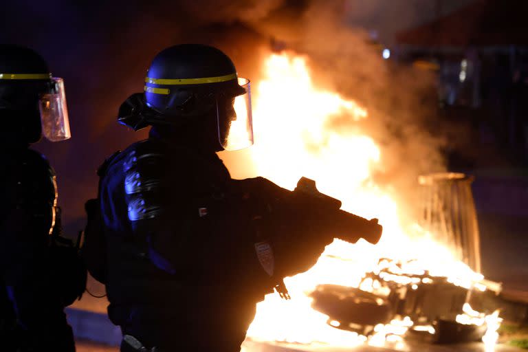 Un agente antidisturbios de la CRS sostiene un lanzabalas defensivo de goma (LBD 40) junto a un fuego provocado por manifestantes en la Plaza de la República durante una manifestación