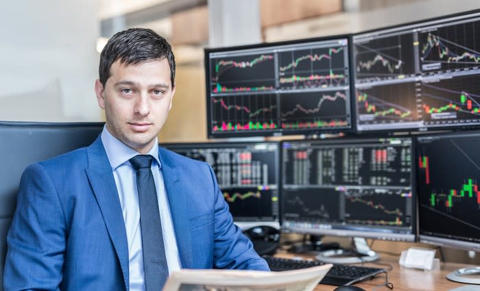 A man in a suit sitting in front of computer screens with stock information on them.