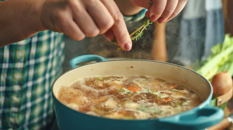 Hands drop thyme into a stockpot