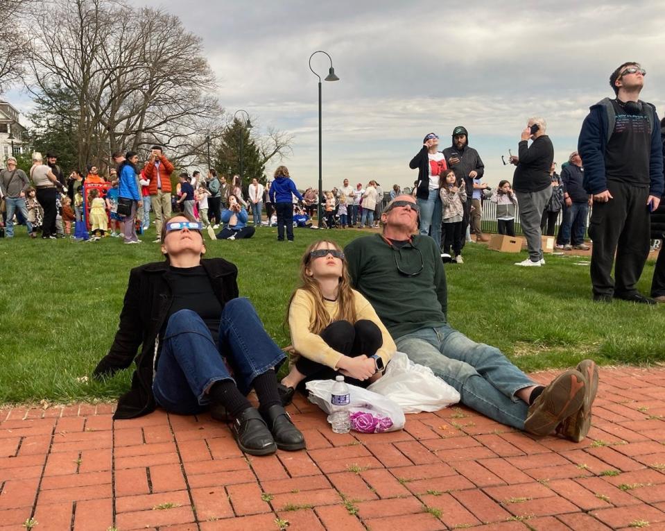 Anne Roder, Jocelyn Mulcahy and Peter Mulcahy glimpse the solar eclipse at its height at 3:34pm April 8, 2024 at the Grundy library in Bristol.