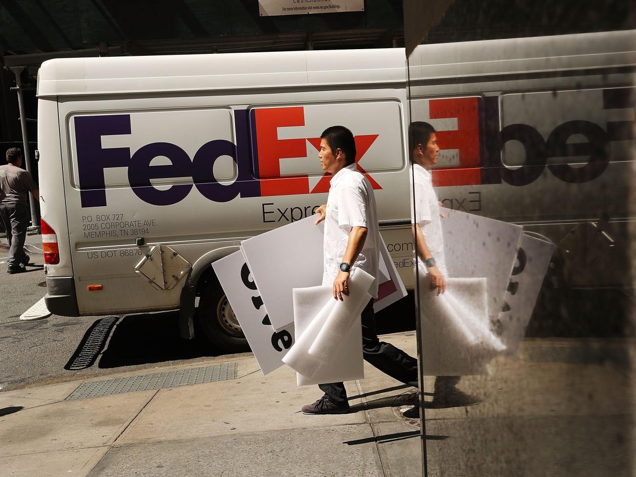 A person carrying strofoam and cardboard walks down the sidewalk past a FedEx delivery truck