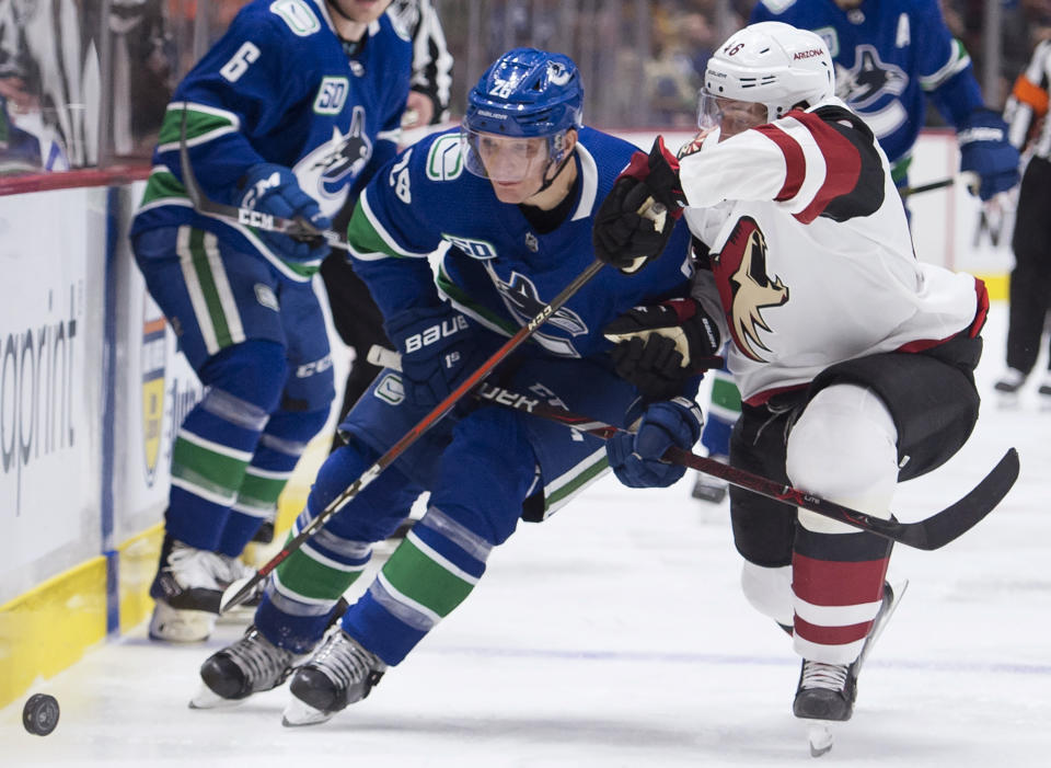 Vancouver Canucks left wing Antoine Roussel (26) fights for control of the puck with Arizona Coyotes defenseman Ilya Lyubushkin (46) during the second period of an NHL hockey game Thursday, Jan. 16, 2020, in Vancouver, British Columbia. (Jonathan Hayward/The Canadian Press via AP)