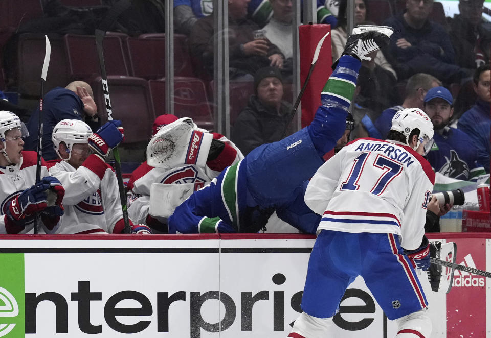 Montreal Canadiens' Josh Anderson (17) checks Vancouver Canucks' Riley Stillman into the Montreal bench during the second period of an NHL hockey game in Vancouver, British Columbia, Monday, Dec. 5, 2022. (Darryl Dyck/The Canadian Press via AP)