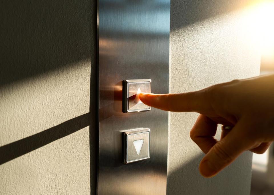 A close up of a finger pressing an elevator button.