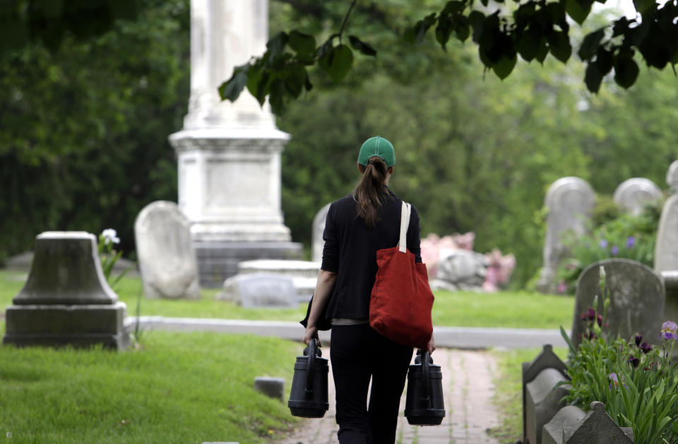 Volunteer Jennifer Walker carries water to the Keen family plot she tends at the Woodlands Cemetery Saturday May 4, 2019 in Philadelphia. The cemeteries of yore existed as much the living as for the dead. And a handful of these 19th century graveyards are restoring the bygone tradition of cemetery gardening. (AP Photo/Jacqueline Larma)