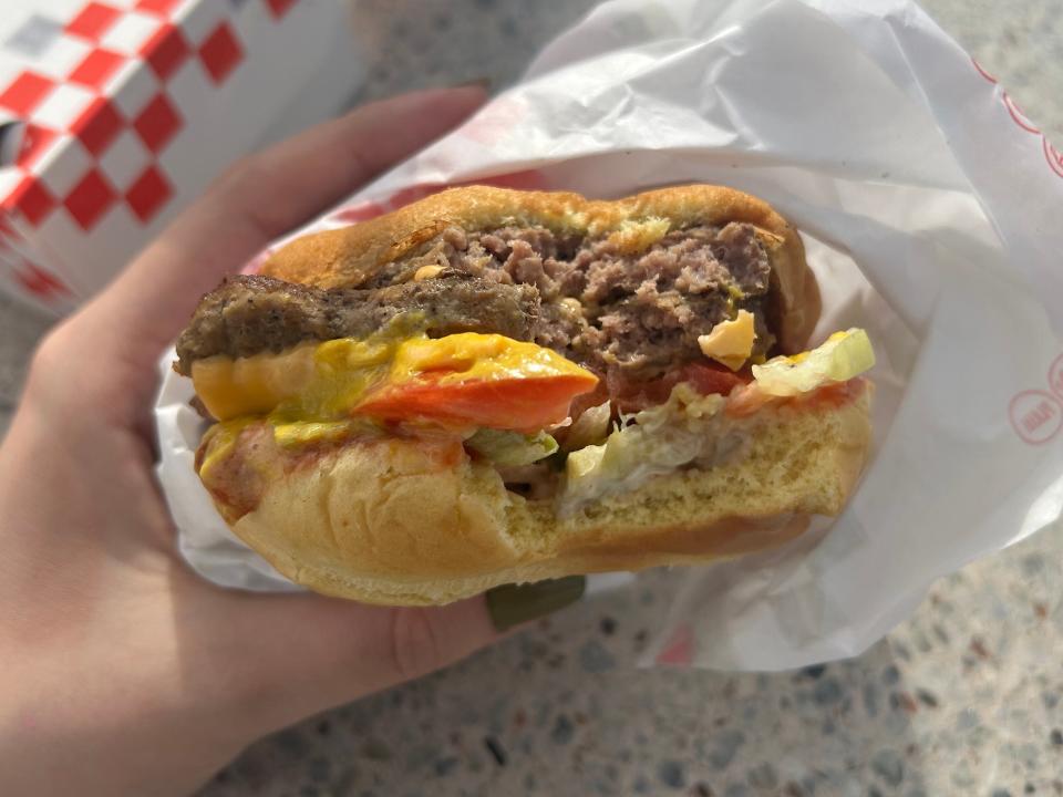 hand holding up a cheeseburger form checkers that has a bite taken out of it