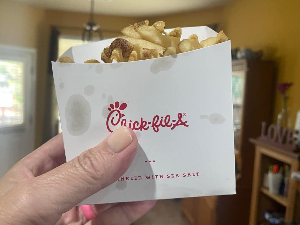 The writer holds a carton of fries from Chick-fil-A with logo on side