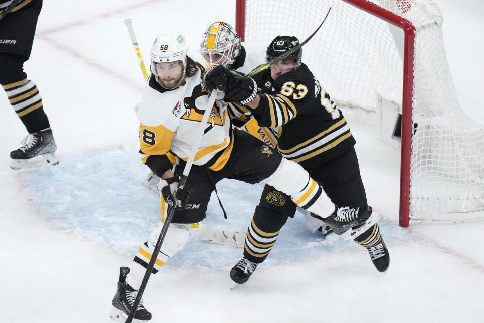 Pittsburgh Penguins defenseman Kris Letang (58) and Boston Bruins left wing Brad Marchand (63) grapple for position in front of Penguins goaltender Alex Nedeljkovic, back center, in the third period of an NHL hockey game, Thursday, Jan. 4, 2024, in Boston. (AP Photo/Steven Senne)