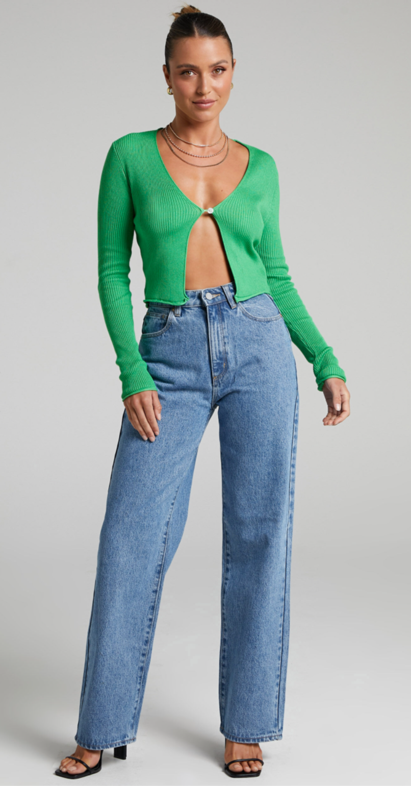 Model with dark hair tied back wears revealing lime green cropped cardigan and jeans.