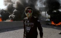 A demonstrator stands near burning tires during ongoing anti-government protests in Tripoli