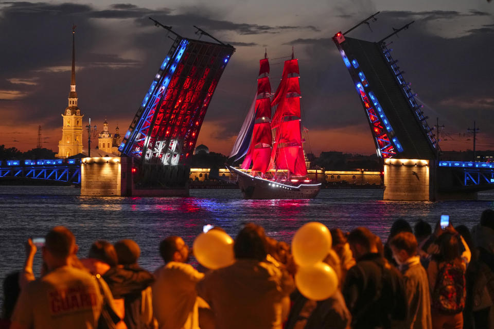 People watch a brig with scarlet sails floating through Dvortsovy (Palace) drawbridge on the Neva River during a rehearsal for the Scarlet Sails festivities marking school graduation in St. Petersburg, Russia, early Friday, June 24, 2022. The Scarlet Sails celebration is a rite of passage both figuratively and literally. Every year, tall ships with glowing red sails make their way down the Neva River in St. Petersburg to honor recent school graduates as they set out on the journey into adulthood. (AP Photo/Dmitri Lovetsky)