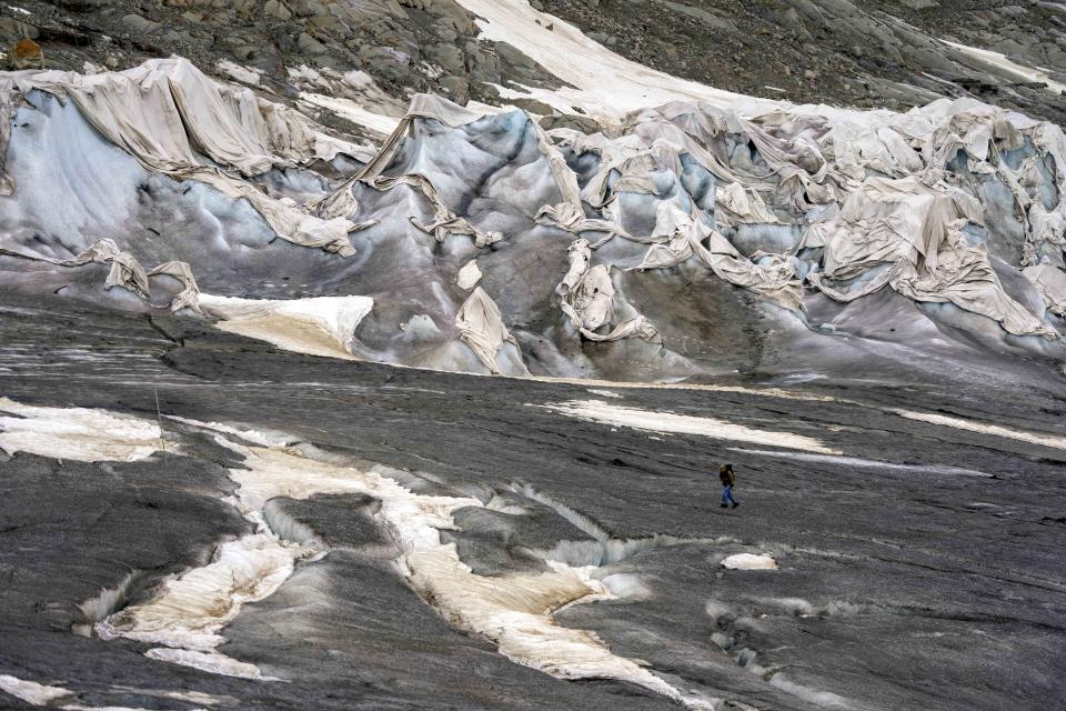 A team member of Swiss Federal Institute of Technology glaciologist and head of the Swiss measurement network 'Glamos', Matthias Huss, passes the Rhone Glacier covered by sheets near Goms, Switzerland, Friday, June 16, 2023. The sheets are just a small scale solution and Alpine glaciers are still expected to vanish by the end of the century. (AP Photo/Matthias Schrader)