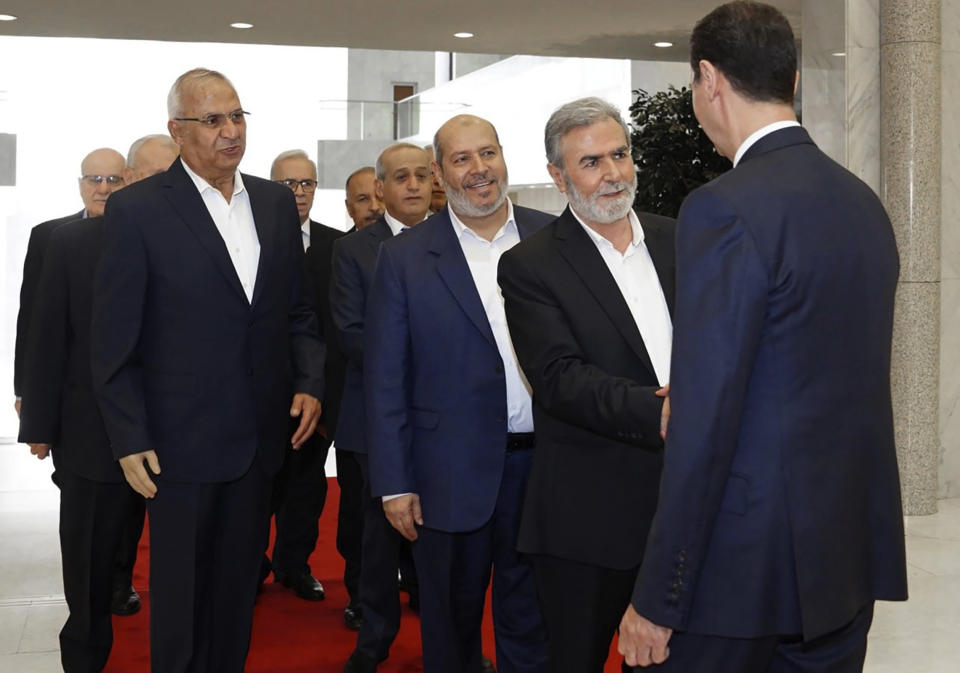 In this photo released by the Syrian official news agency SANA, shows Syrian President Bashar Assad, right, shakes hands with Ziad Nakhaleh, leader of the Palestinian Islamic Jihad group, as Khalil al-Hayeh, a senior figure in Hamas' political branch, third right, and others wait to greet the president, in Damascus, Syria, Wednesday, Oct. 19, 2022. Al-Hayeh was one of two senior officials from the Palestinian militant Hamas group who visited Syria's capital on Wednesday for the first time since they were forced to leave the war-torn country a decade ago over backing armed opposition fighters. (SANA via AP)