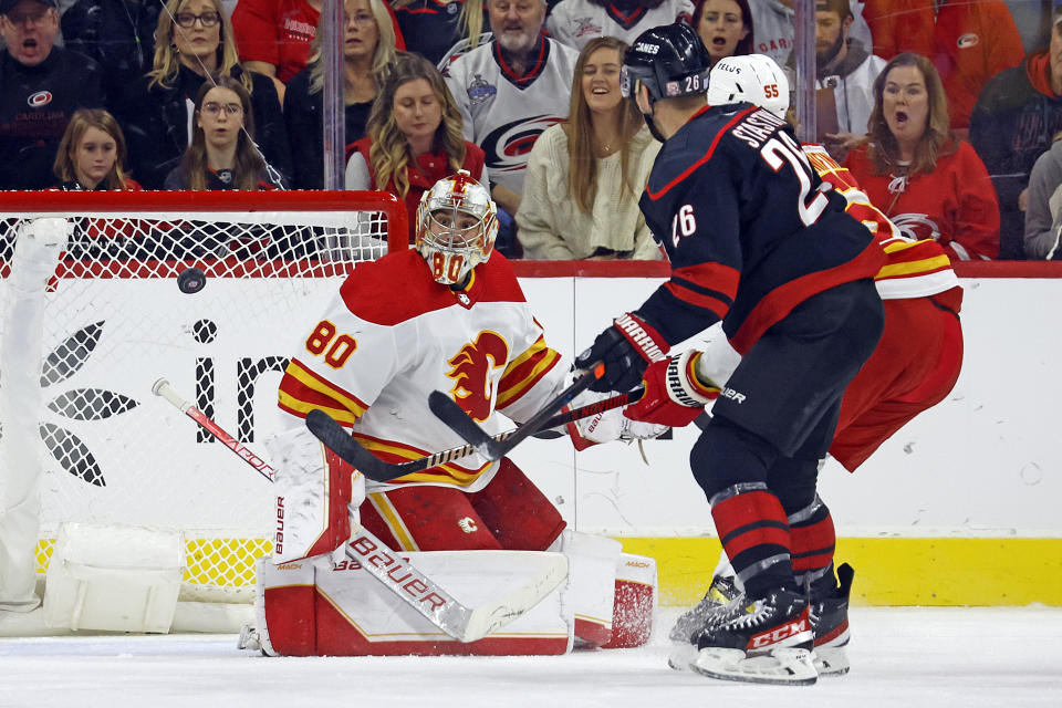 Calgary Flames goaltender Dan Vladar (80) watches the puck as Carolina Hurricanes' Paul Stastny (26) and Flames' Noah Hanifin (55) skate nearby during the first period of an NHL hockey game in Raleigh, N.C., Saturday, Nov. 26, 2022. (AP Photo/Karl B DeBlaker)