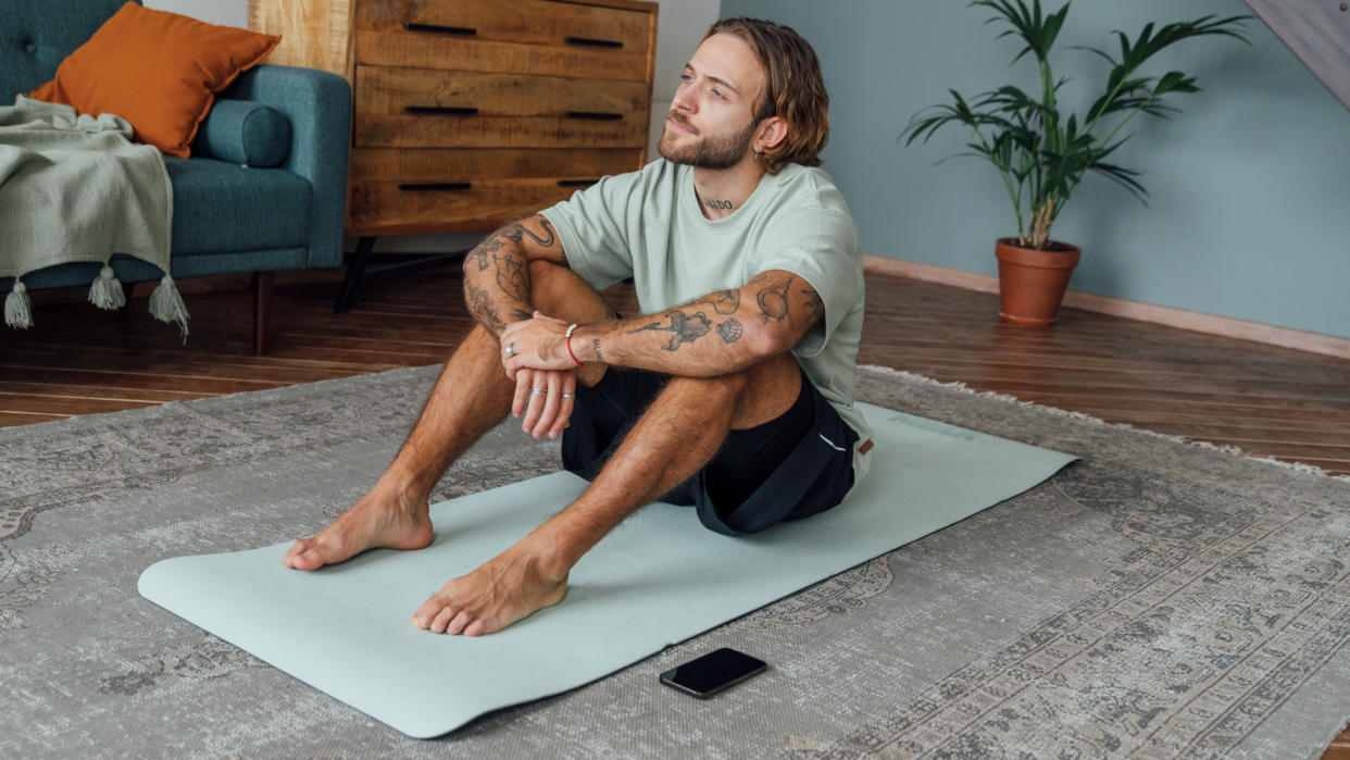  A man sitting on a yoga mat. 