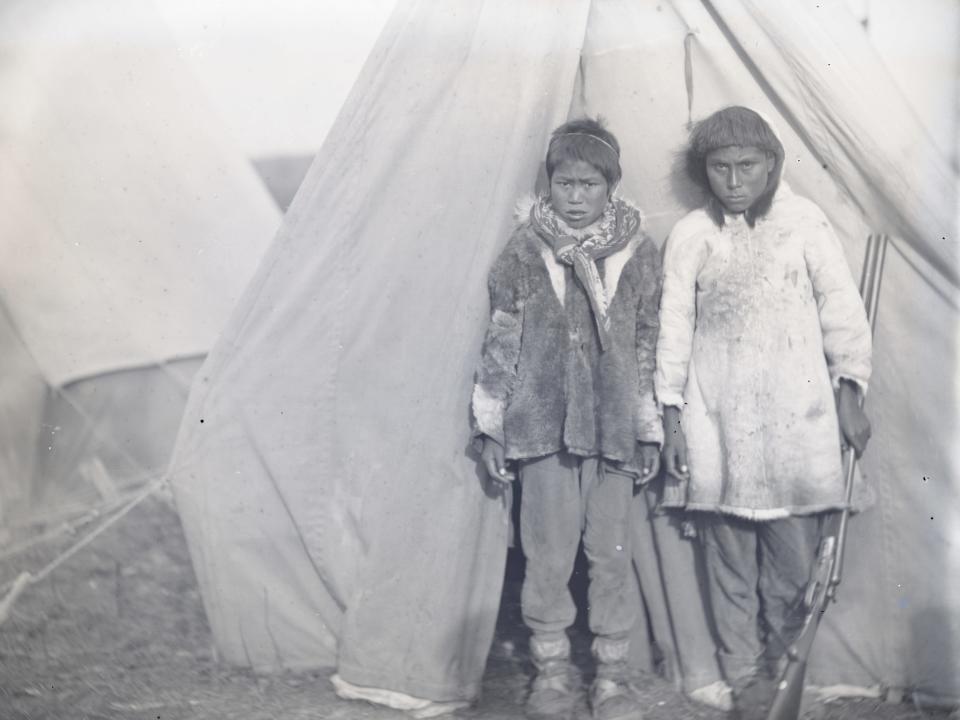 Northern Alaska Exploring Expedition, 1884-1886. Two Inuit children in front of tent, one holding a rifle. Exploration of the Kobuk River and northern parts of Alaska, led by Lieutenant George M. Stoney of the U.S. Navy. Specimens were collected for the United States National Museum. Artist Unknown.