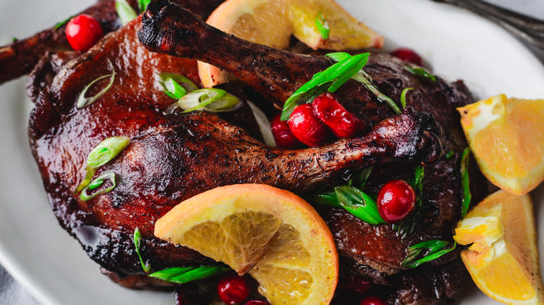 Close up on duck legs, cranberries and orange on white plate
