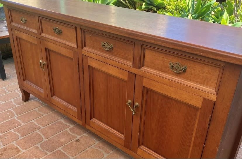 A dated timber buffet photographed outside before upcycling with metal handles, four drawers and four doors.