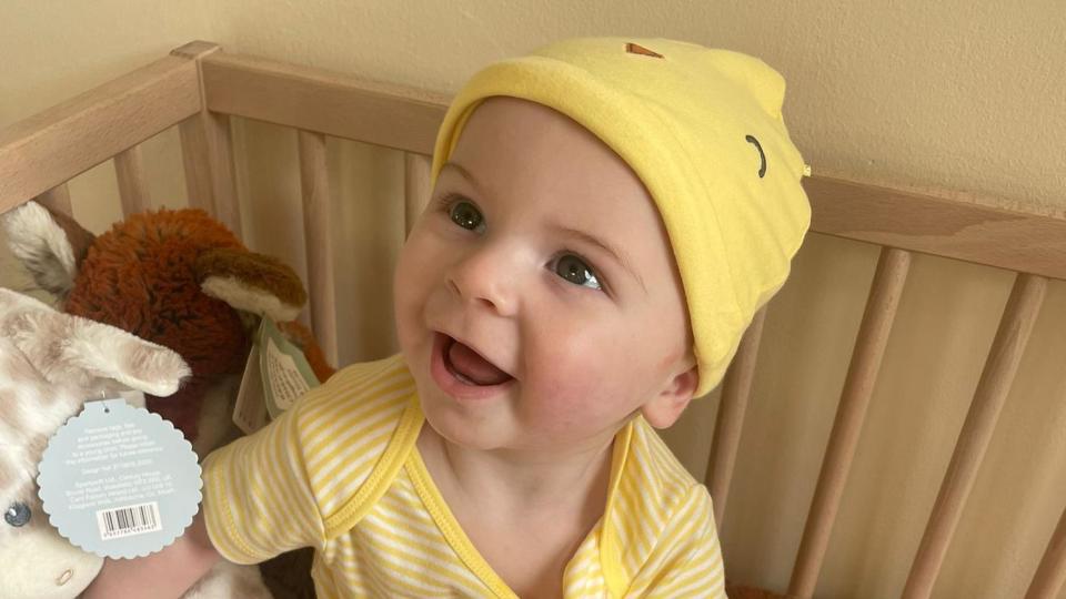 A young boy in a yellow stripey shirt and hat smiles at the camera